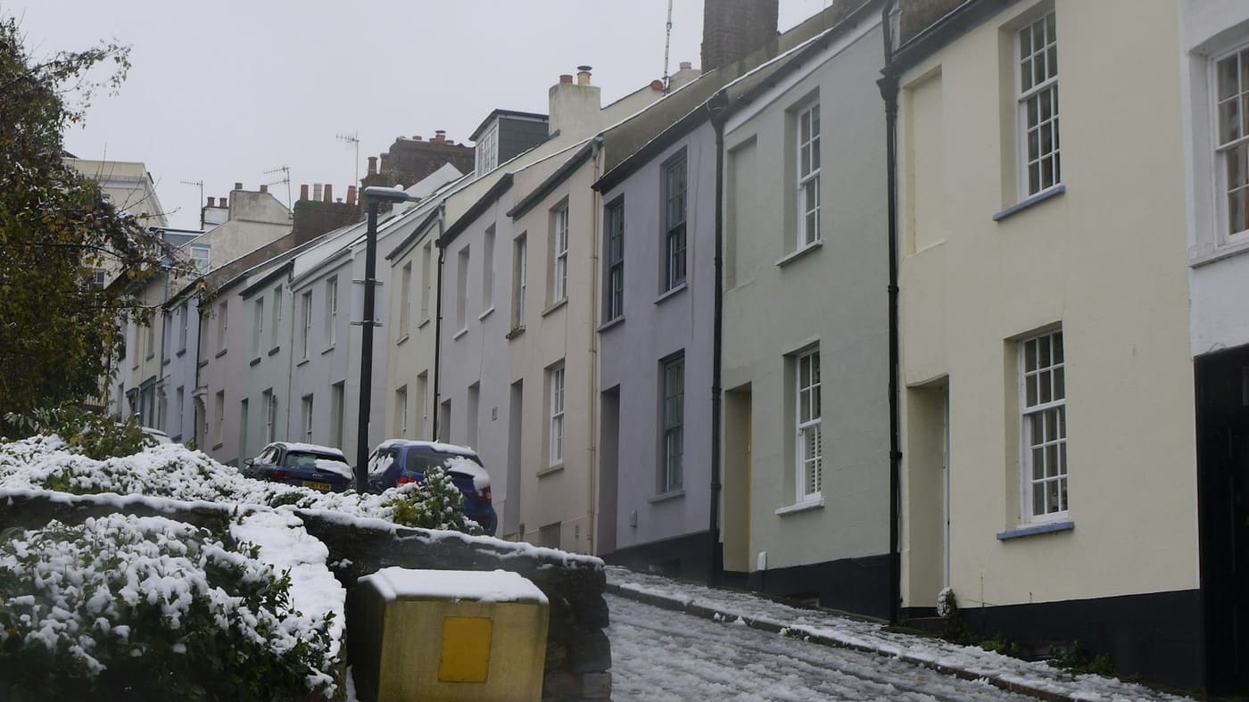 A snowy terraced street with a yellow grit bin