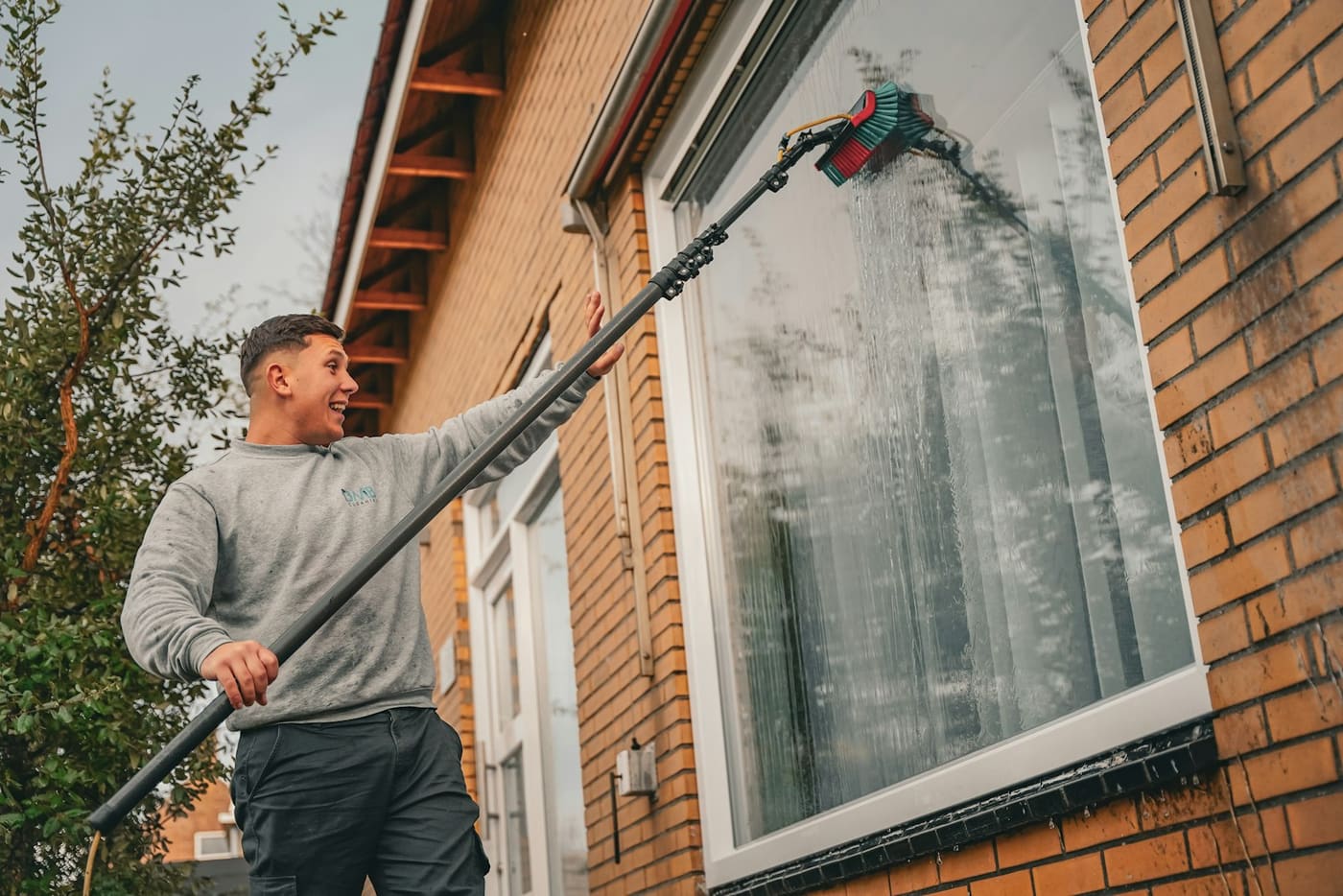A window cleaner using a water-fed pole on a brick house